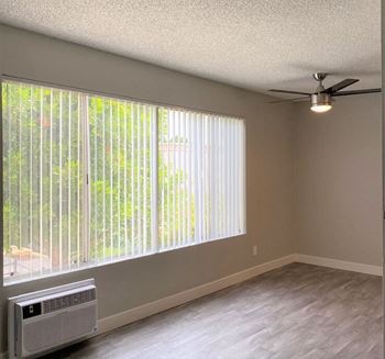 An empty living room with a large window and a ceiling fan